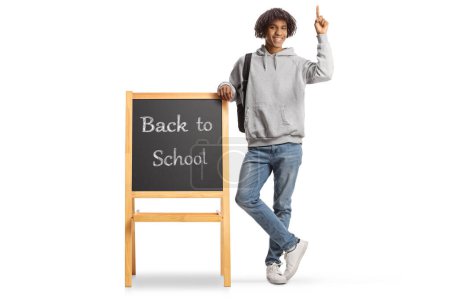 Photo for African american male student leaning on a blackboard with text back to school and pointing up isolated on white background - Royalty Free Image