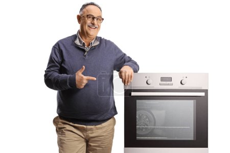 Photo for Smiling mature man leaning on an oven and pointing isolated on white backgroun - Royalty Free Image