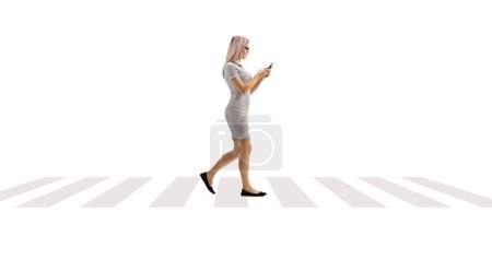 Téléchargez les photos : Jeune femme marchant et utilisant un smartphone à un passage pour piétons isolé sur fond blanc - en image libre de droit