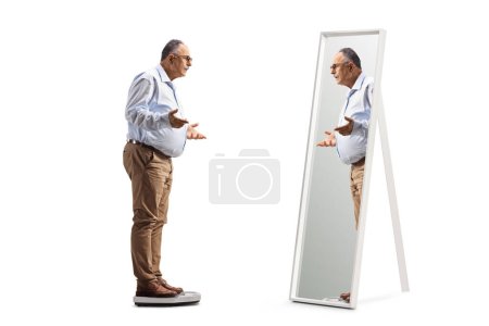 Photo for Full length shot of a mature man standing on a measuring scale in front of a mirror isolated on white background - Royalty Free Image