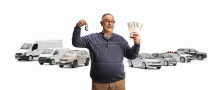 Téléchargez les photos : Homme mûr souriant tenant une clé et des piles d'argent devant de nombreux véhicules isolés sur fond blanc - en image libre de droit