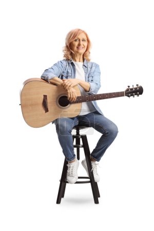 Photo for Female mature artist with an acoustic guitar sitting on a chair isolated on white background - Royalty Free Image