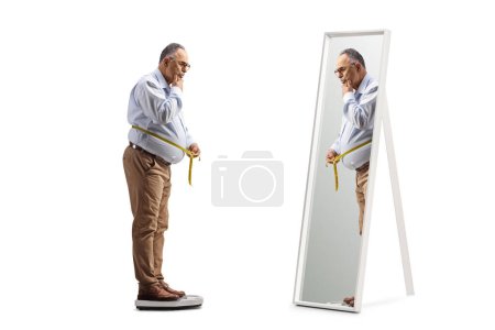 Photo for Full length shot of a pensive mature man on a scale measuring waist in front of a mirror isolated on white background - Royalty Free Image