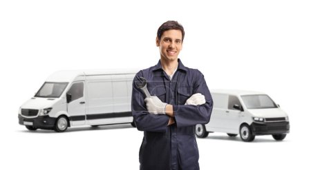 Photo for Young worker in a uniform holding a wrench in front of two white vans isolated on white background - Royalty Free Image