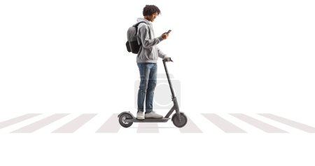 Téléchargez les photos : Africain américain mâle chevauchant un scooter électrique sur piéton traversant et en utilisant smartphone isolé sur fond blanc - en image libre de droit