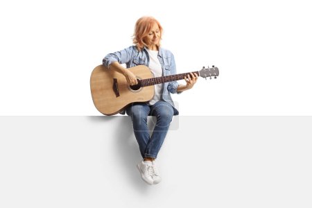 Foto de Retrato de larga duración de una mujer sentada en un panel tocando una guitarra acústica aislada sobre fondo blanco - Imagen libre de derechos