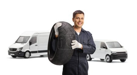 Téléchargez les photos : Mécanicien automobile tenant un pneu devant deux fourgonnettes blanches isolées sur fond blanc - en image libre de droit