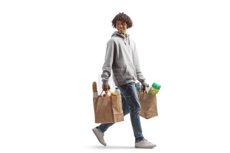 Foto de Largura completa de un joven afroamericano llevando bolsas de comestibles caminando y mirando hacia atrás aislado sobre fondo blanco - Imagen libre de derechos