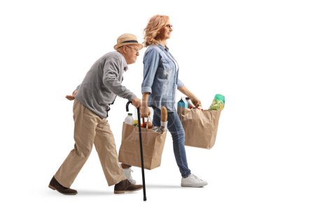 Foto de Foto de perfil completo de un anciano caminando con un bastón y una mujer llevando bolsas aisladas sobre fondo blanco - Imagen libre de derechos