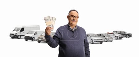 Téléchargez les photos : Homme mûr tenant des piles d'argent devant des véhicules garés isolés sur fond blanc - en image libre de droit