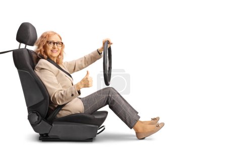 Photo for Mature woman sitting in a car seat holding a steering wheel and gesturing thumbs up isolated on white background - Royalty Free Image