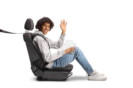 Téléchargez les photos : Jeune homme afro-américain assis dans un siège auto avec une ceinture de sécurité et agitant isolé sur fond blanc - en image libre de droit