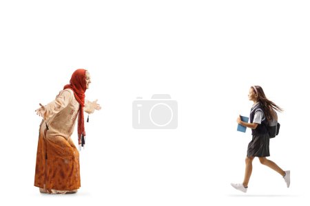 Téléchargez les photos : Écolière courant vers une femme en vêtements ethniques musulmans isolés sur fond blanc - en image libre de droit