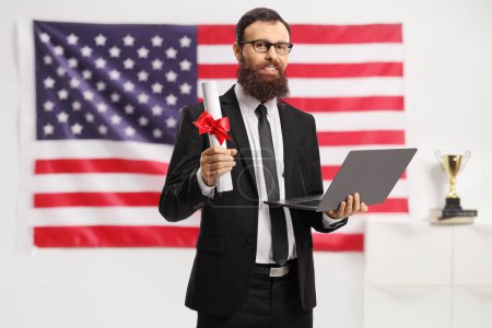Photo for Bearded american man in a suit holding a diploma and a laptop computer in front of the USA flag - Royalty Free Image