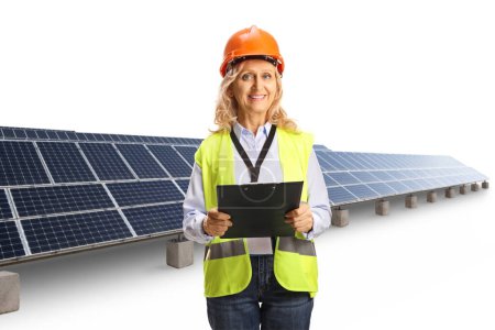 Foto de Ingeniera femenina con chaleco de seguridad y casco sonriente y de pie frente a una granja de paneles solares aislada sobre fondo blanco - Imagen libre de derechos