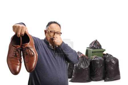 Foto de Hombre maduro sosteniendo un par de zapatos apestosos cerca de un cubo de basura aislado sobre fondo blanco - Imagen libre de derechos