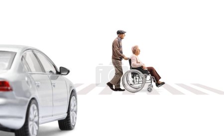 Photo for Full length profile shot of an elderly man pushing an elderly woman in a wheelchair at a pedestrian crossing and car waiting isolated on white background - Royalty Free Image
