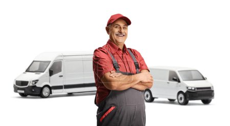 Photo for Van driver in a uniform smiling at camera and posing in front of two white vans isolated on white background - Royalty Free Image