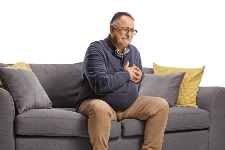 Téléchargez les photos : Homme mûr assis sur un canapé et ayant des symptômes de crise cardiaque isolé sur fond blanc - en image libre de droit