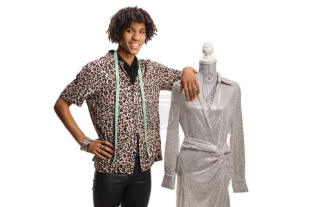 Photo for Young african american male fashion designer with a measuring tape leaning on a doll mannequin with a dress isolated on white background - Royalty Free Image