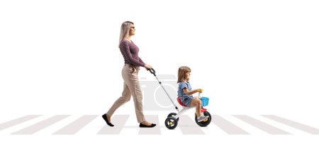 Téléchargez les photos : Mère poussant un enfant sur un tricycle à un passage pour piétons isolé sur fond blanc - en image libre de droit