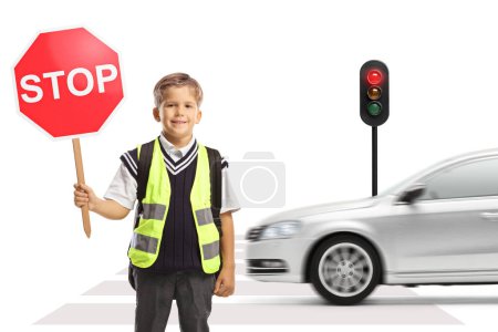 Photo for Schoolboy with a safety vest and a stop traffic sign standing at a pedestrian crossing with car driving in the back - Royalty Free Image