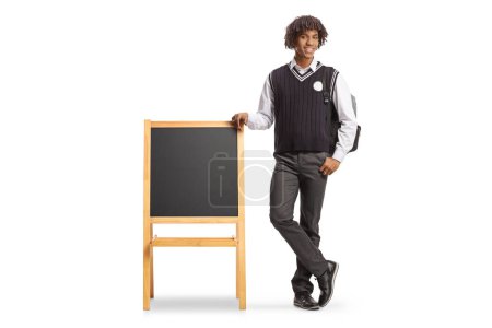Téléchargez les photos : Portrait complet d'un étudiant afro-américain de sexe masculin en uniforme appuyé sur un tableau noir isolé sur fond blanc - en image libre de droit