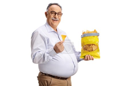 Foto de Alegre hombre maduro comiendo patatas fritas de tortilla y sonriendo aislado sobre fondo blanco - Imagen libre de derechos