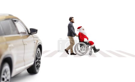 Téléchargez les photos : Vue de profil pleine longueur d'un homme poussant Père Noël claus dans un fauteuil roulant à un passage pour piétons isolé sur fond blanc - en image libre de droit
