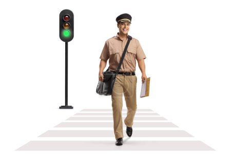 Photo for Full length portrait of a postman walking at a pedestrian crossing and a traffic light flashing green isolated on white background - Royalty Free Image