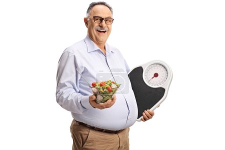 Foto de Hombre maduro sosteniendo una ensalada y una báscula aislada sobre fondo blanco - Imagen libre de derechos