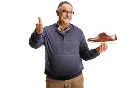 Photo for Mature man holding a brown leather shoe and gesturing thumbs up isolated on white background - Royalty Free Image