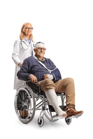 Foto de Hombre maduro con un brazo roto y vendaje en la cabeza sentado en una silla de ruedas y doctora de pie detrás aislada sobre fondo blanco - Imagen libre de derechos