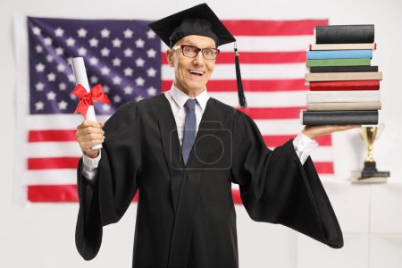 Foto de Anciano con diploma y un montón de libros sonriendo a la cámara delante de una bandera de EE.UU. - Imagen libre de derechos