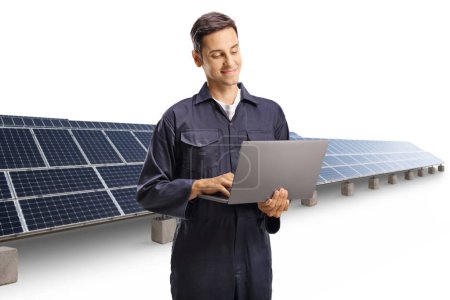 Photo for Young male worker in a uniform with a laptop computer standing in front of a solar field isolated on white background - Royalty Free Image