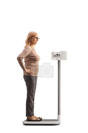 Photo for Full length profile shot of a woman checking her weight on a professional medical scale isolated on white background - Royalty Free Image