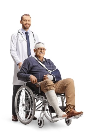 Foto de Hombre maduro con un brazo roto y vendaje en la cabeza sentado en una silla de ruedas y un médico de pie detrás aislado sobre fondo blanco - Imagen libre de derechos