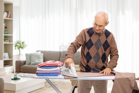 Foto de Hombre mayor alegre planchando la ropa en casa en una sala de estar - Imagen libre de derechos