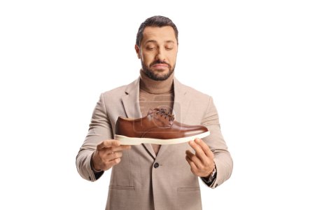 Téléchargez les photos : Jeune homme tenant une chaussure en cuir marron et la regardant isolée sur fond blanc - en image libre de droit
