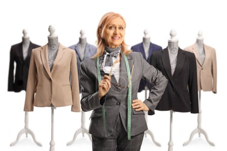 Photo for Female fashion designer holding a tape and posing in front of mannequin dolls with suits isolated on white background - Royalty Free Image