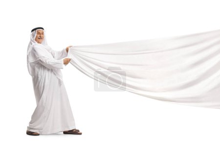 Téléchargez les photos : Arabe en vêtements traditionnels tirant un morceau de tissu blanc isolé sur fond blanc - en image libre de droit
