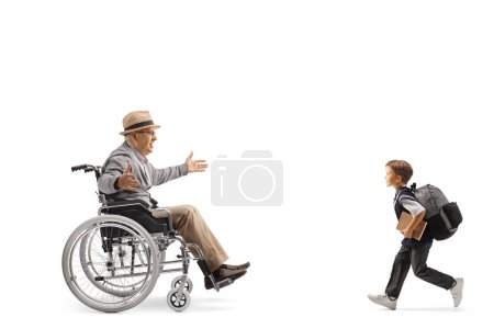 Foto de Foto de perfil completo de un colegial corriendo hacia un anciano en silla de ruedas aislado sobre fondo blanco - Imagen libre de derechos