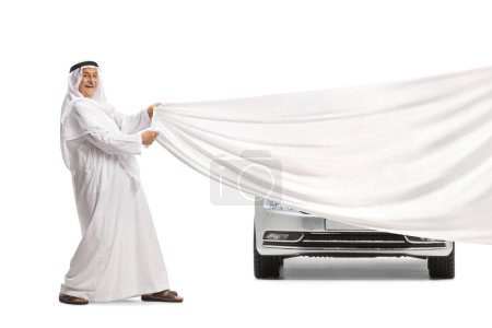 Téléchargez les photos : Homme arabe dans le dédachi traditionnel tenant un morceau de tissu blanc devant une voiture isolée sur fond blanc - en image libre de droit