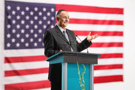 Téléchargez les photos : Homme d'affaires mature donnant un discours sur un podium devant le drapeau des États-Unis - en image libre de droit