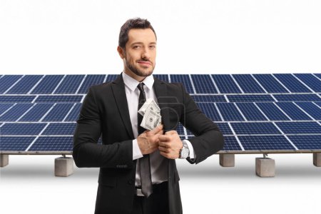 Téléchargez les photos : Homme d'affaires mettre de l'argent dans sa poche et debout devant des panneaux solaires isolés sur fond blanc - en image libre de droit