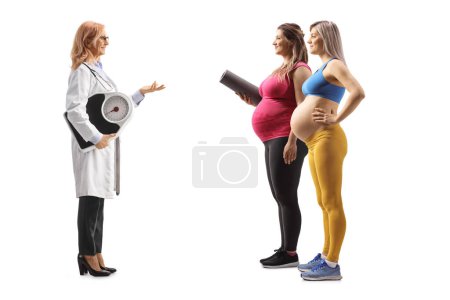 Téléchargez les photos : Plan complet du profil d'une femme médecin tenant une balance de poids et parlant à deux femmes enceintes isolées sur fond blanc - en image libre de droit