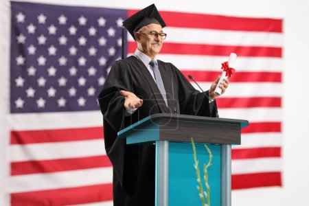 Photo for Dean giving a speech and holding a certificate with the USA flag in the background - Royalty Free Image