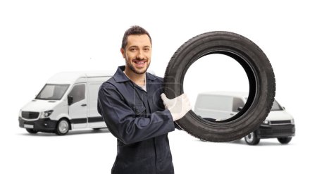 Foto de Mecánico automático sosteniendo un neumático frente a dos furgonetas blancas aisladas sobre fondo blanco - Imagen libre de derechos