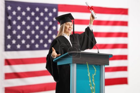 Photo for Female student of honor holding a certificate at a podium in front of the USA flag - Royalty Free Image