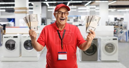 Photo for Mature store manager holding money and smiling inside an electrical appliance shop - Royalty Free Image